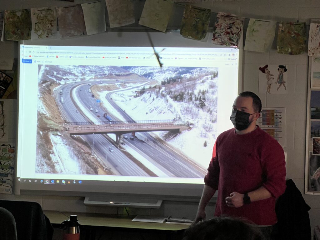Austin standing in front of a slide that shows the animal bridge that was built across Interstate 80.